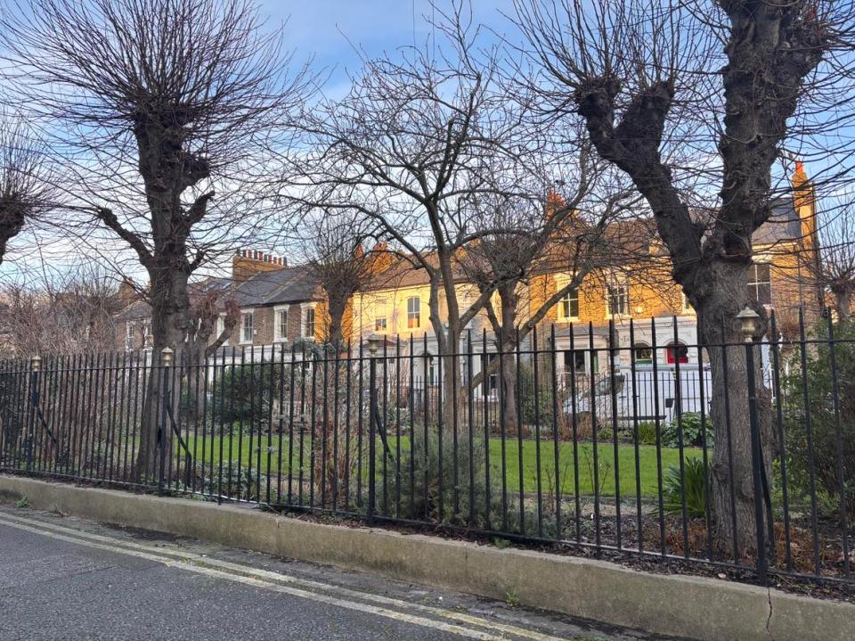 Row of houses behind a fence and bare trees.