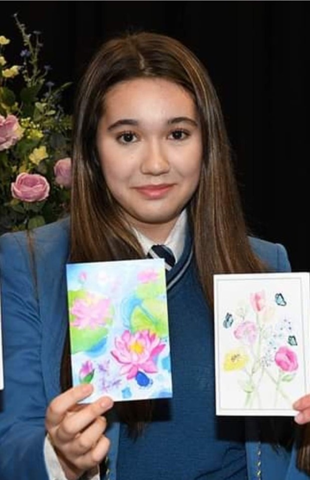 Girl holding two watercolor paintings of flowers.