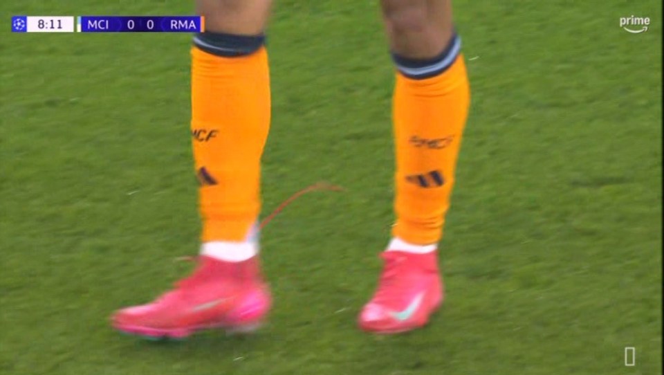 Soccer player's legs and feet in orange socks and pink cleats.