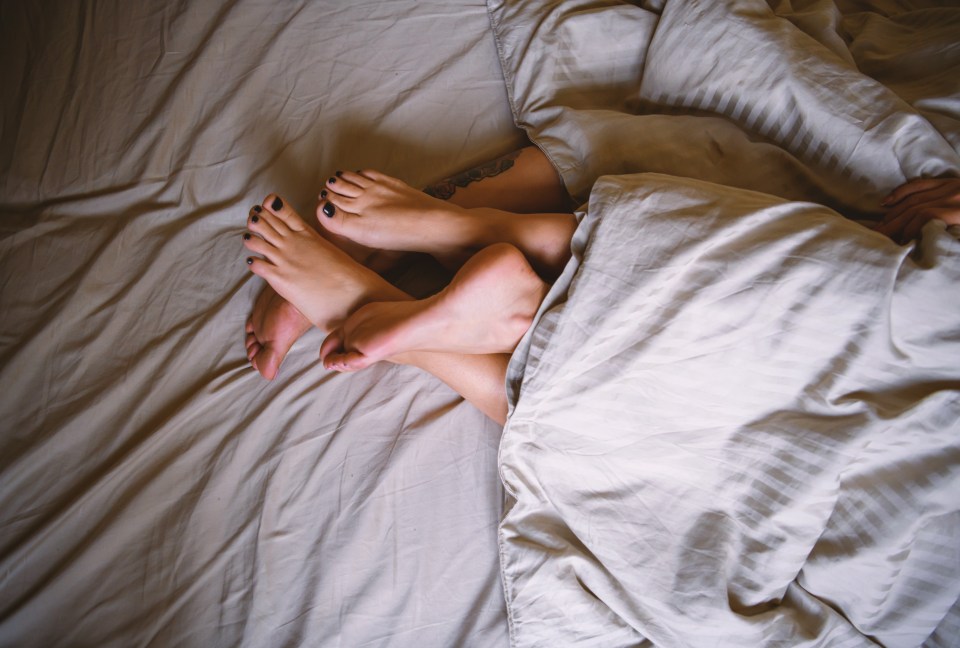 Lesbian couple's intertwined legs under a duvet.