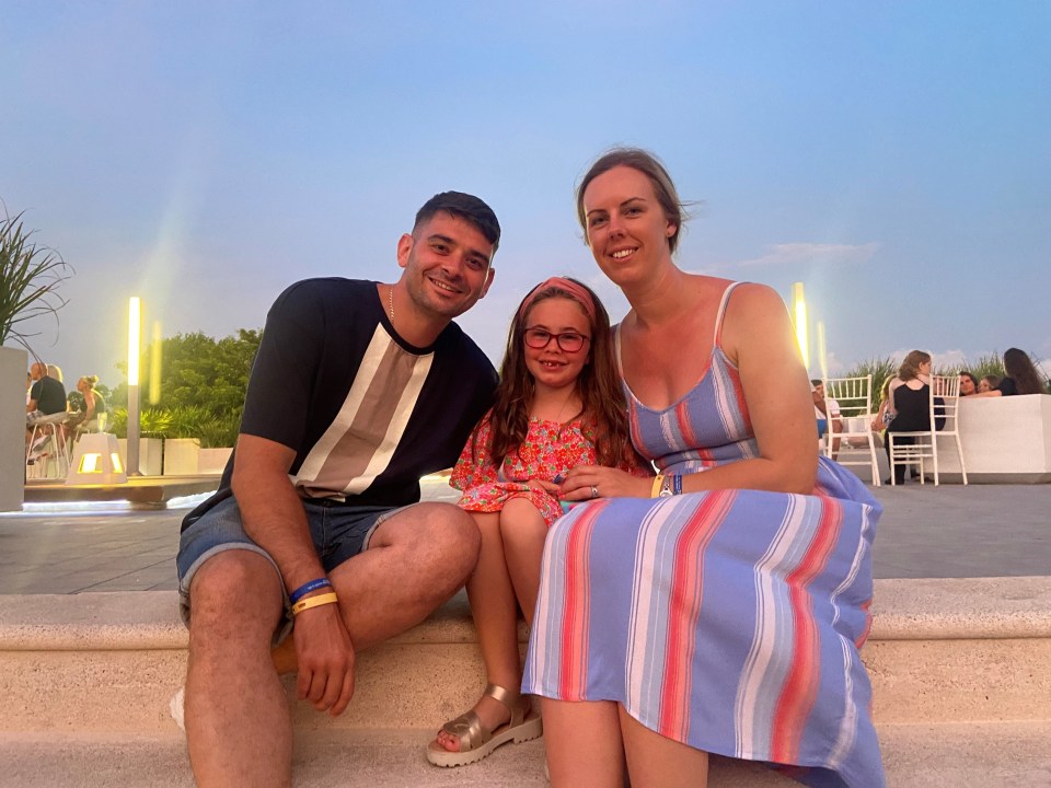 Family photo of a man, woman, and young girl sitting on steps at dusk.