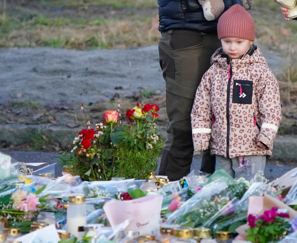 A young girl stands near a memorial of flowers and candles.