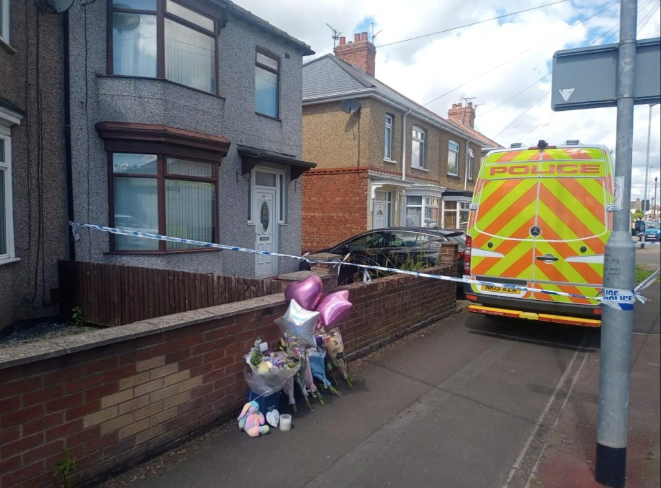 Crime scene photo showing a house with police tape and a memorial.