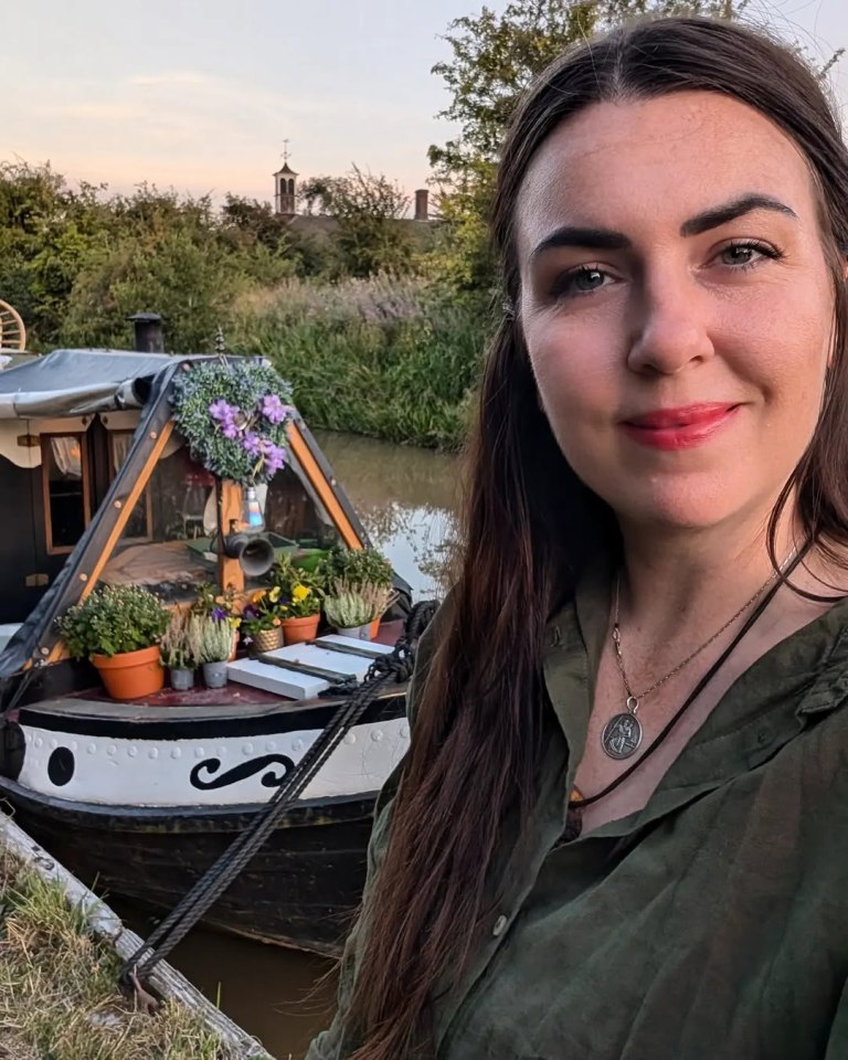 Woman standing by canal boat with potted plants.