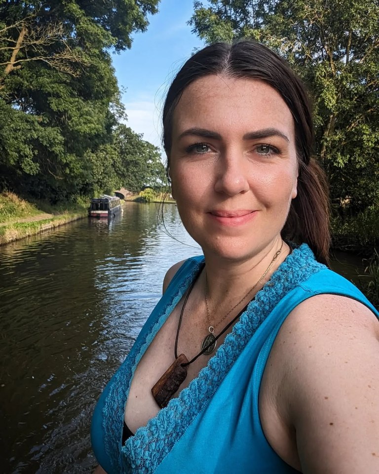 Woman in teal top by canal with boat in background.