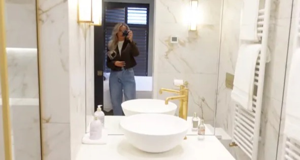 A woman taking a selfie in a marble bathroom with gold fixtures.