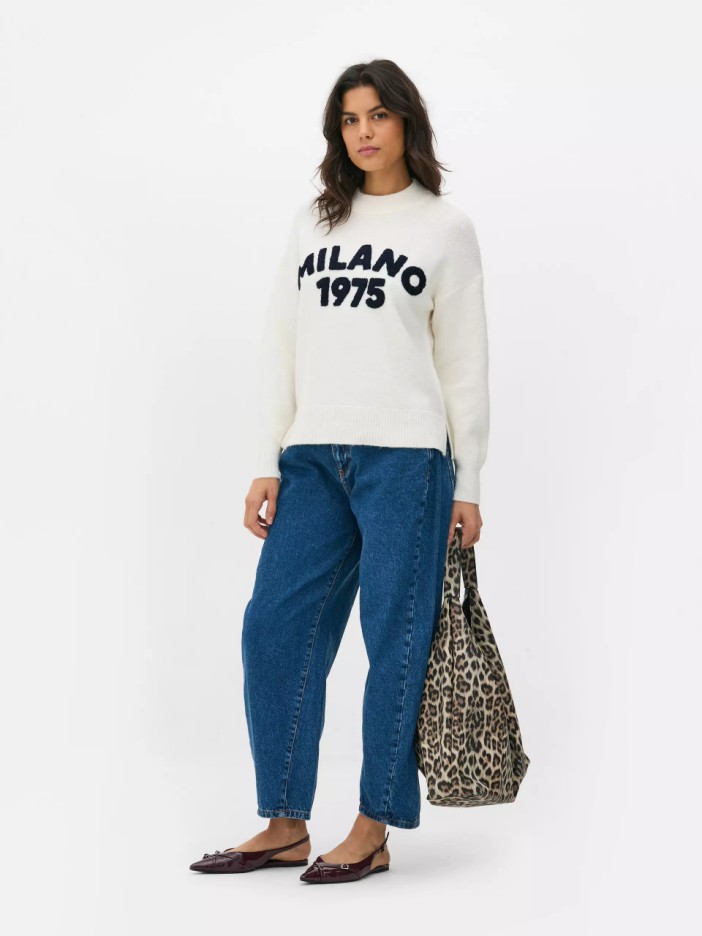 Woman wearing a cream Milano 1975 sweater, blue jeans, and leopard print tote bag.