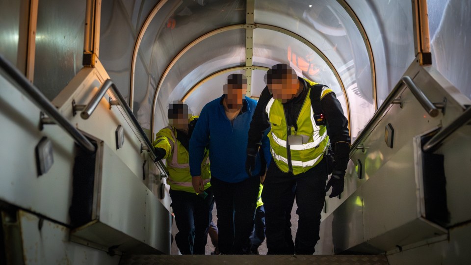 People descending a covered staircase, escorted by security personnel.