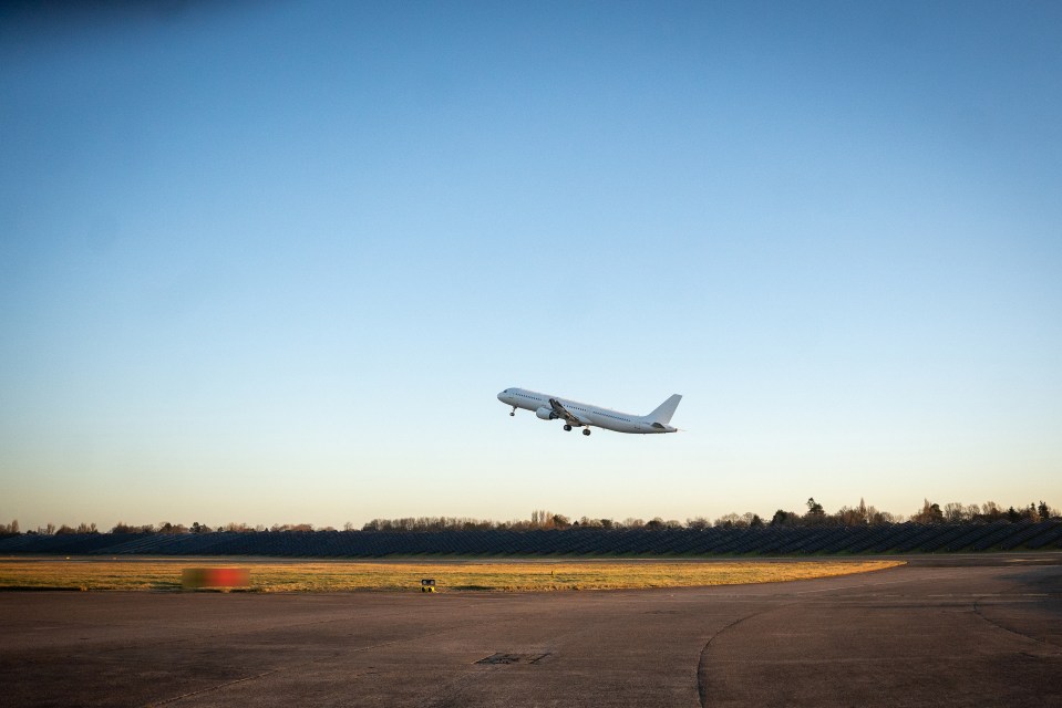 Airplane taking off over a solar panel field.