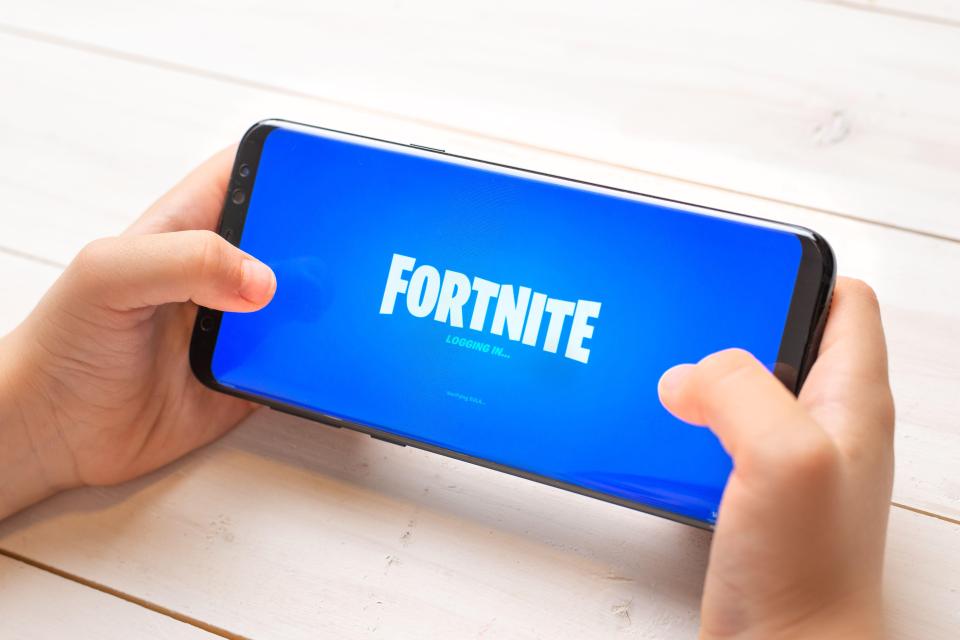 Child's hands holding a smartphone displaying the Fortnite loading screen.