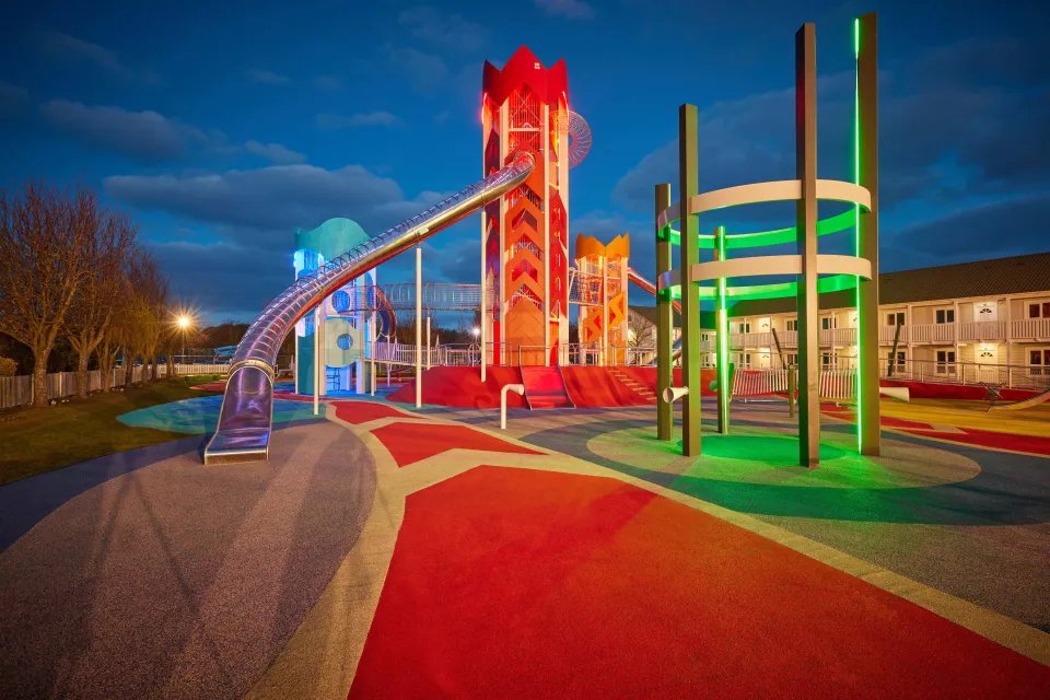 Modern playground at night with colorful structures and slides.