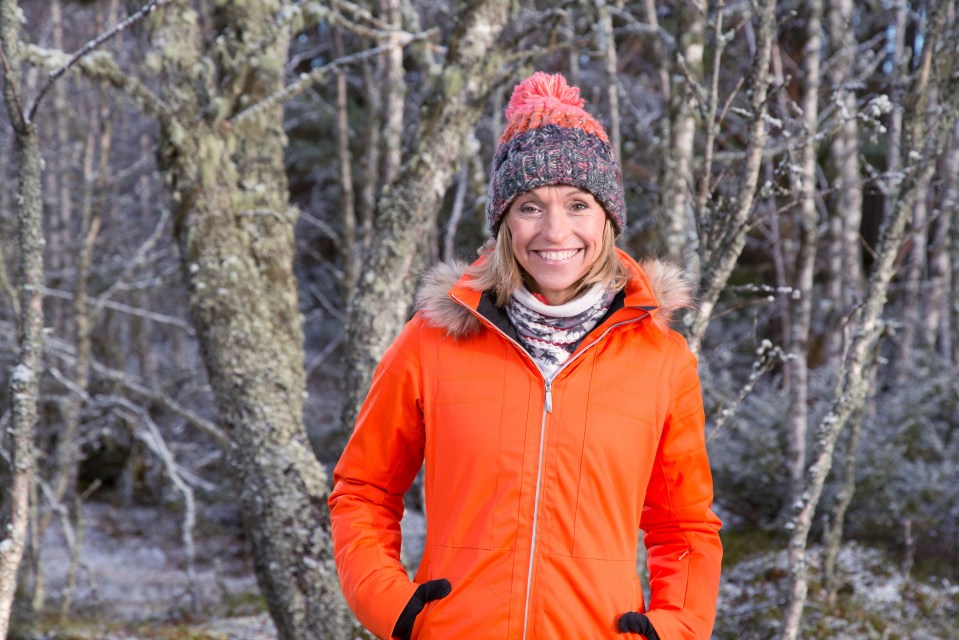 Woman in orange jacket smiling in snowy woods.