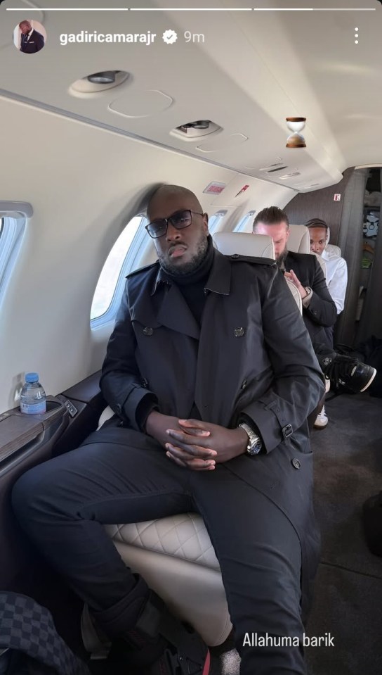 Man in a black coat seated on a private jet.