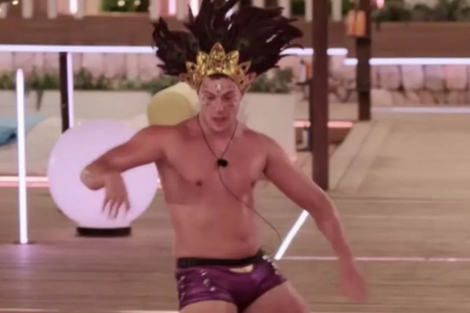 Man in feathered headdress and purple shorts dancing.