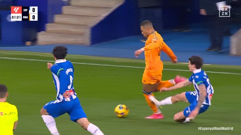 Soccer player in orange jersey dribbling the ball past a player in a blue jersey.