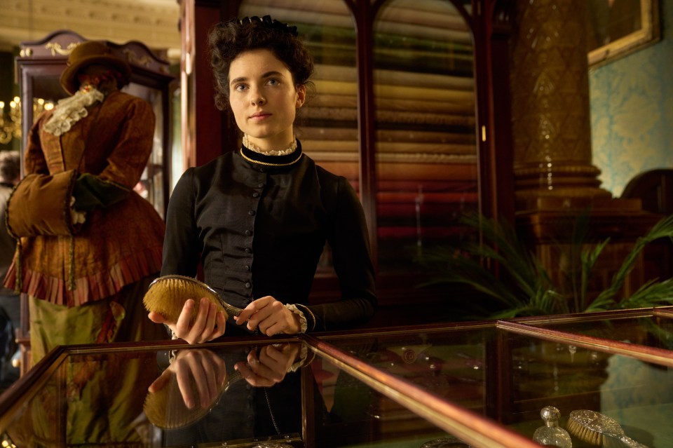 Woman in period dress holding a hairbrush behind a glass display case.