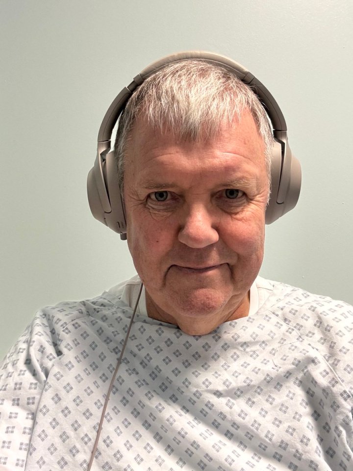 Man in hospital gown wearing headphones.