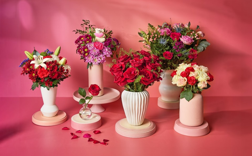 Arrangement of five bouquets of flowers in various vases on pink stands.