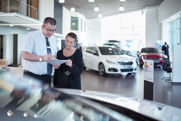 Salesman and customer reviewing paperwork at a car dealership.