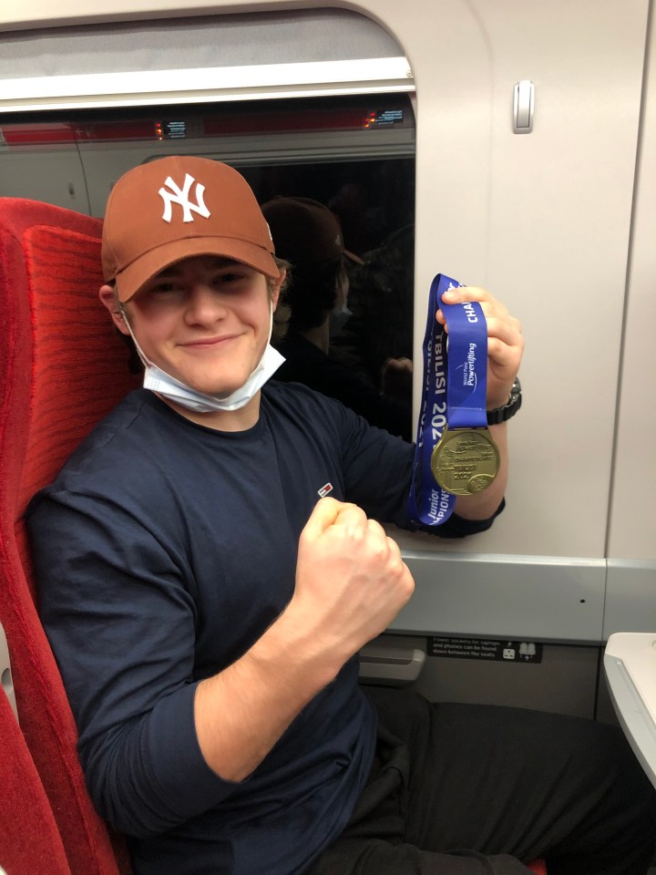 A young man on a train shows off his gold medal from the 2021 Tbilisi Junior World Para Powerlifting Championships.