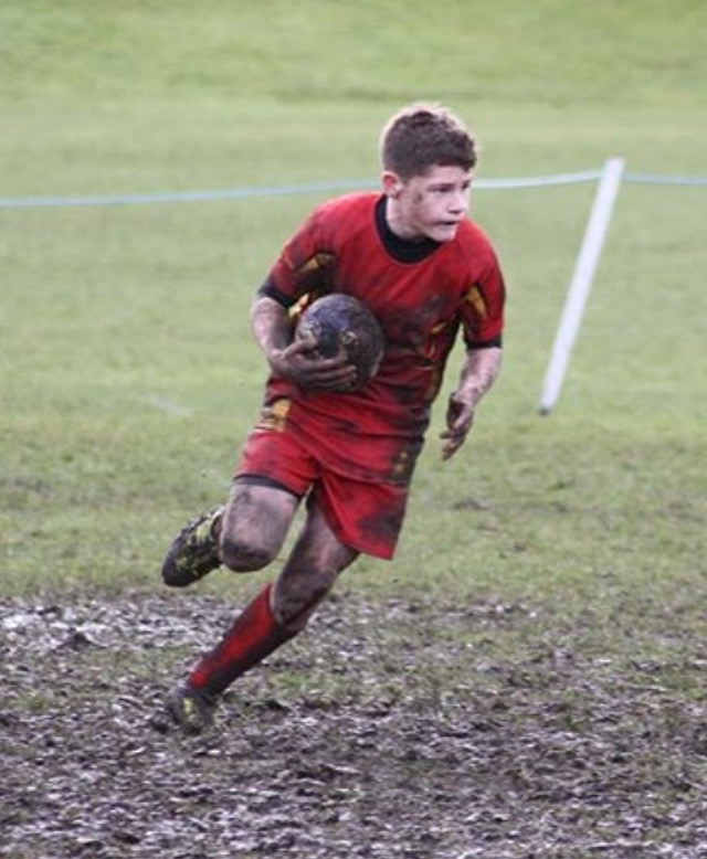 Muddy rugby player running with the ball.