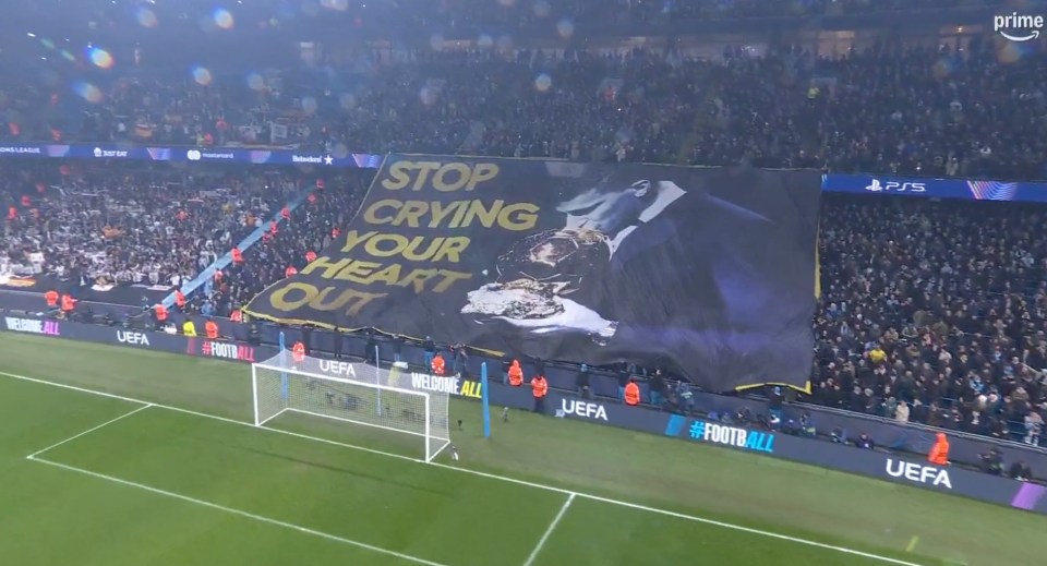 Stadium crowd unfurling a banner that reads "Stop crying your heart out".