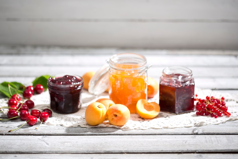 Three jars of jam: cherry, apricot, and red currant.  Fresh fruit is arranged nearby.