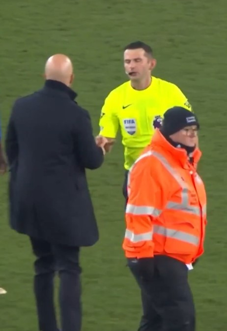 Soccer coach, referee, and stadium official on the field.