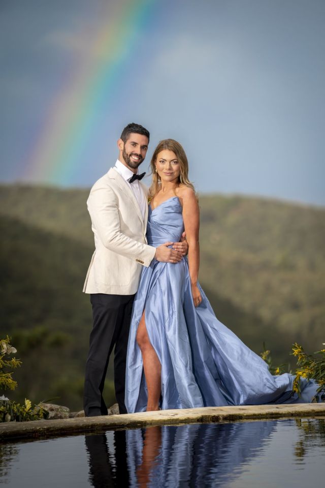 Couple posing by a pool with a rainbow in the background.