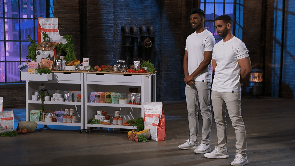 Two men standing in front of a display of dog food and ingredients.