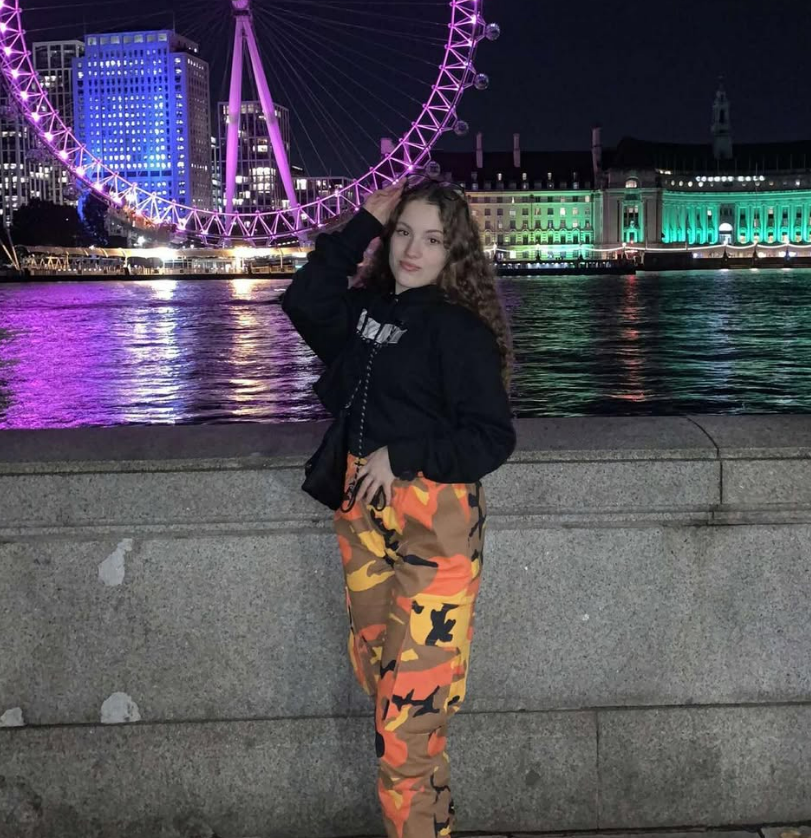 Girl in orange camouflage pants posing in front of the London Eye at night.