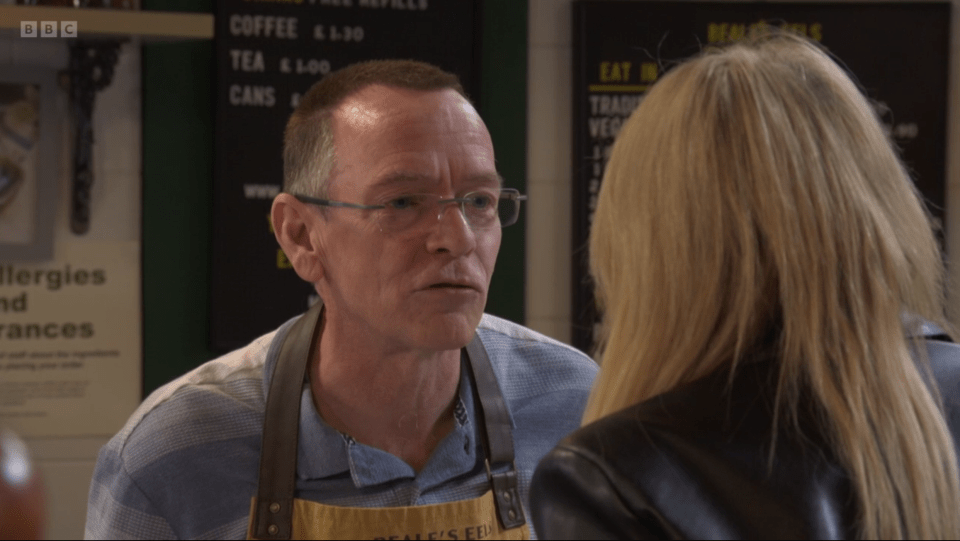 Screenshot of a man in an apron talking to a woman.