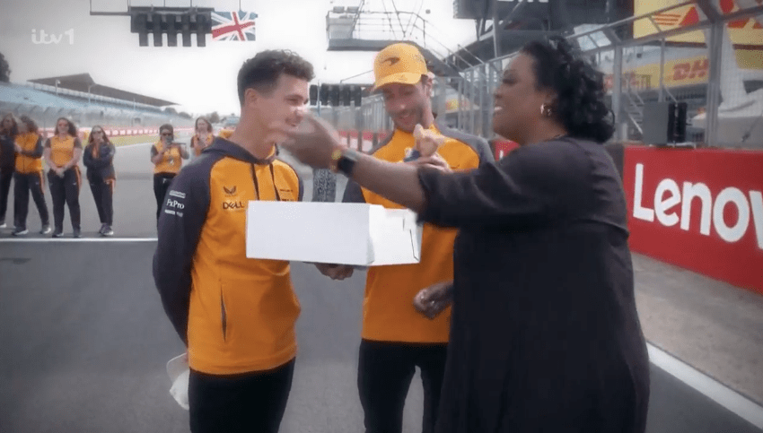 A woman presenting two men with a box at a racetrack.