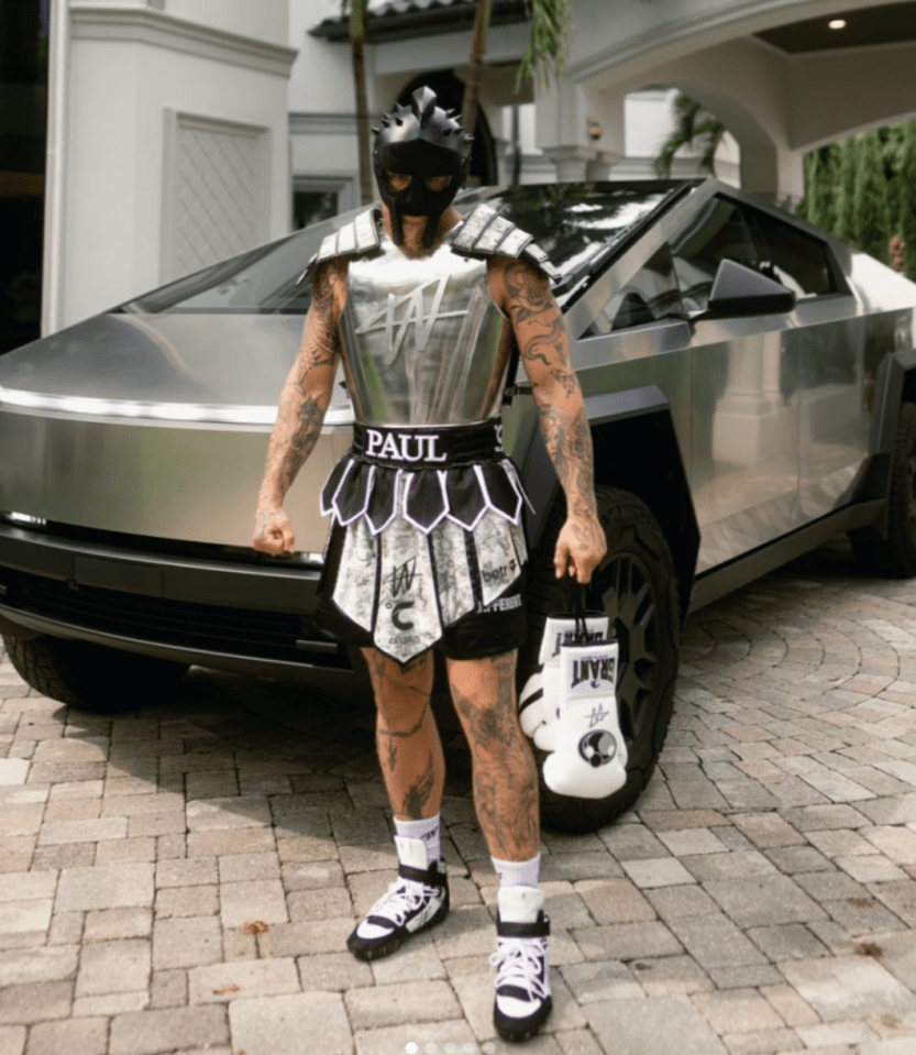 A tattooed boxer in a gladiator costume stands by a Tesla Cybertruck.