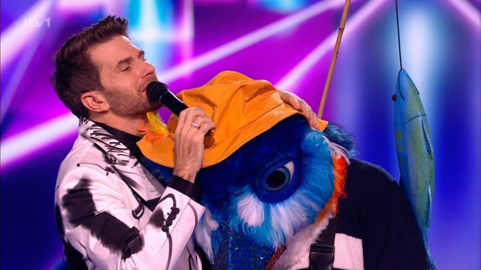 A man singing while hugging a blue bird costume.