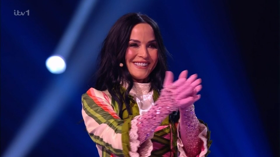 A woman in a colorful striped jacket and sparkly gloves applauds.