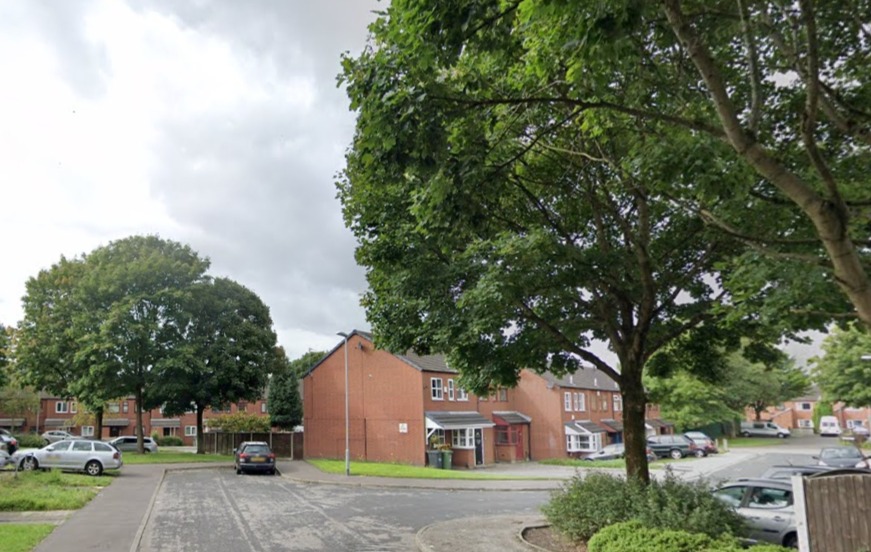 Residential street with parked cars and brick houses.