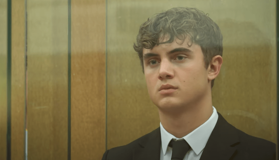 Young man in a suit behind glass.