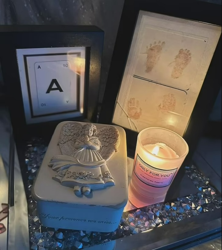 Memorial display with baby's footprints, angel figurine, and candle.