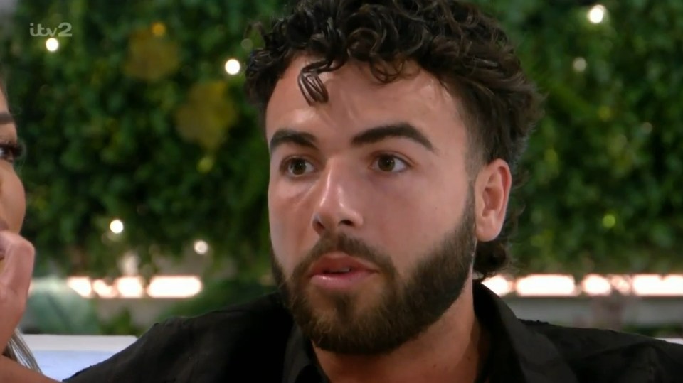 Screenshot of a man with curly hair and a beard, looking pensive.