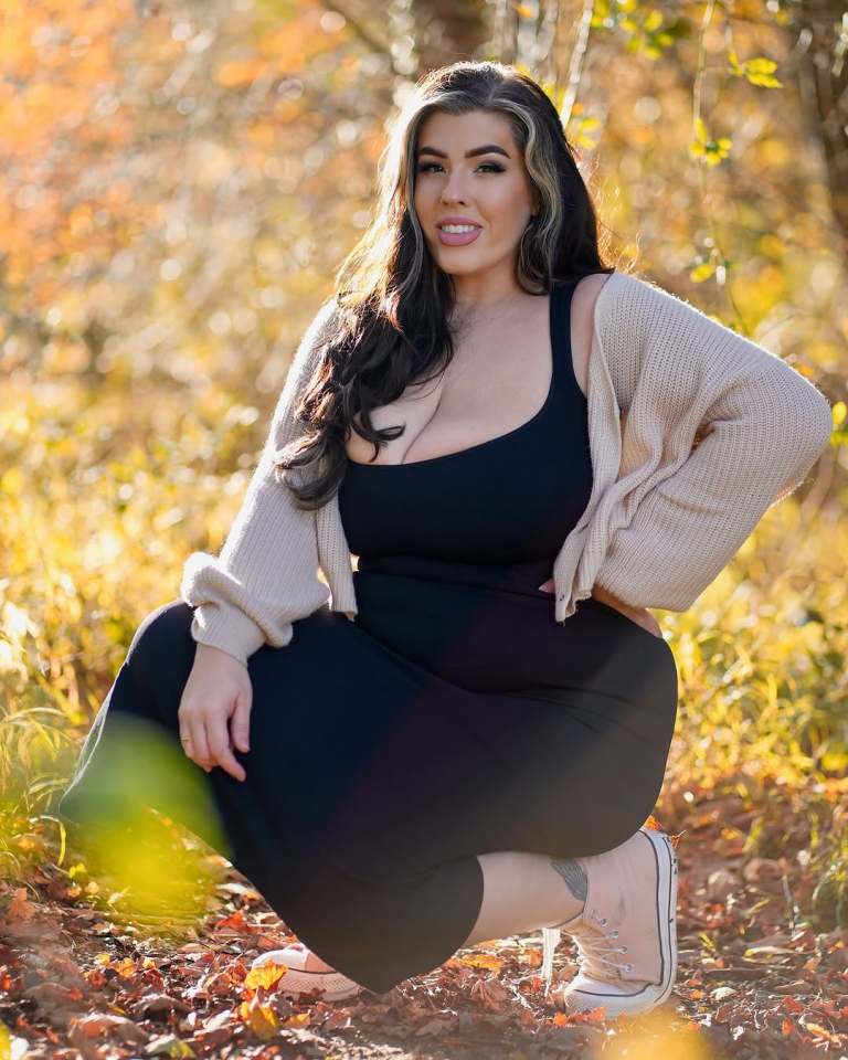 Woman in black dress and beige cardigan squatting in autumn leaves.