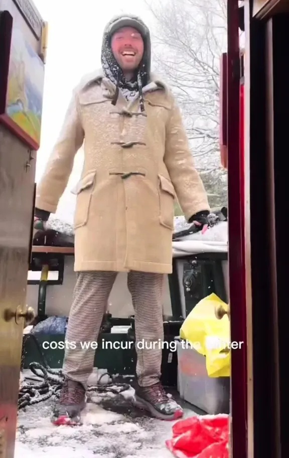 Man in a snow-covered coat smiling in a snowy doorway.