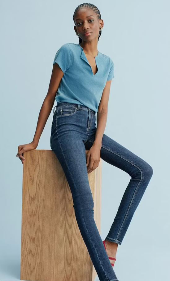 Woman in jeans and a blue shirt sitting on a wooden block.