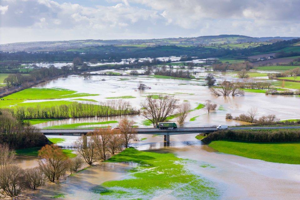 Aerial view of flooded fields and a river with vehicles crossing a bridge.