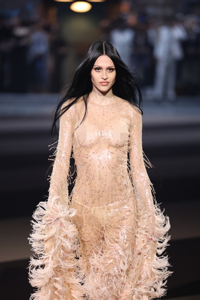 Amelia Gray Hamlin walking the runway in a sheer, sequined gown with feather trim at Milan Fashion Week.