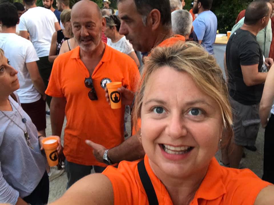 Woman in orange shirt taking a selfie with people in the background.