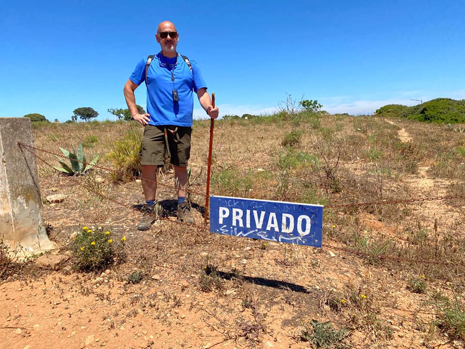 Man standing by a "privado" sign in a dry, grassy field.