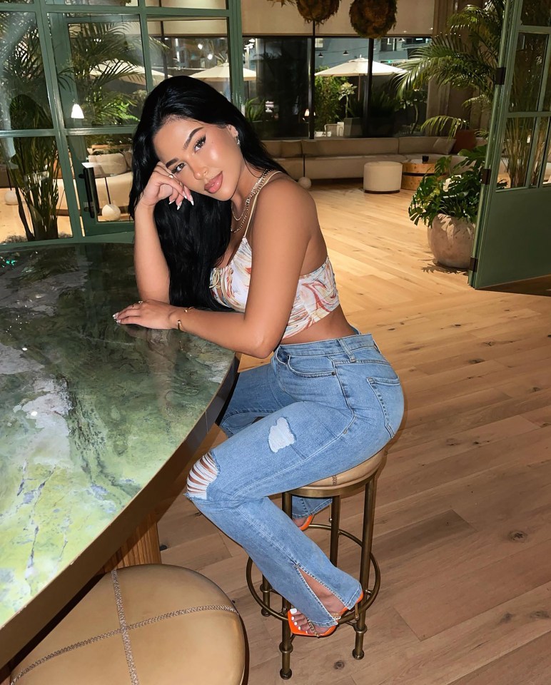 Woman in jeans and a crop top sitting at a bar.