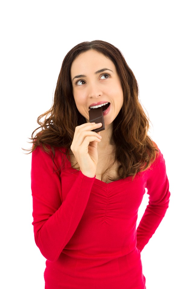 Woman in red shirt biting a piece of dark chocolate.