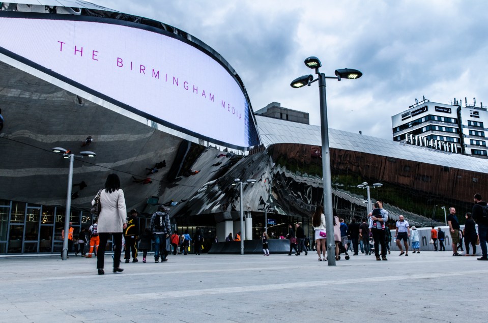 People walking in front of Birmingham New Street Station on an overcast day.